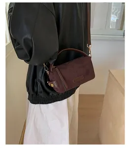 Detalle del bolso bandolera de ante marrón oscuro con herrajes dorados y un asa
