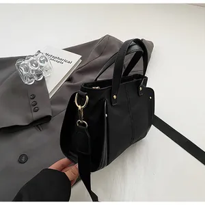 Detalle de bolso tote de cuero negro con remaches metálicos y correa ancha ajustable