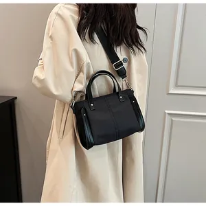 Detalle de bolso tote negro de nailon con correa ancha sobre una gabardina color beige
