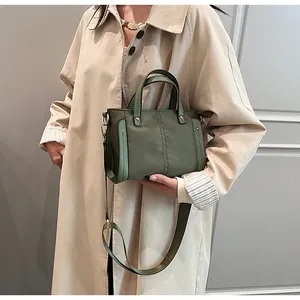 Detalle del bolso tote de nailon verde hierba con correa ancha sobre gabardina beige