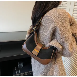 Detalle del bolso de hombro en ante negro y marrón con cadena dorada y hebilla metálica