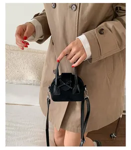 Detalle de un mini bolso bandolera de ante negro con lazo decorativo y hebilla plateada