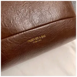Détail macro du sac en cuir ciré marron foncé avec logo doré et coutures fines