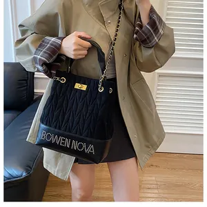 Detalle del bolso saco acolchado negro con diseño de letras metálicas y cadena dorada