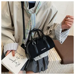 Detalle del bolso cilíndrico negro con asas de cuero y logotipo blanco en el frente