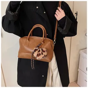 Sac à main marron avec pendentif cœur léopard porté avec un long manteau noir élégant