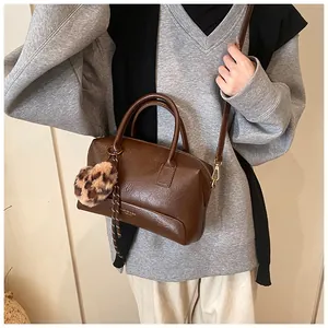 Vue latérale du sac Boston en cuir marron foncé avec poignées et pompon léopard