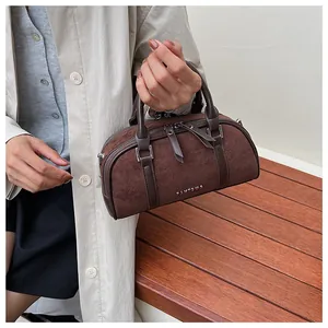 Detalle de un bolso Boston de ante marrón oscuro con logo y textura vintage mate