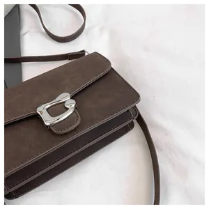 Detalle de un bolso bandolera de ante marrón mate con una hebilla metálica plateada