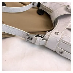 Detalle de bolso de hombro blanco con relieve de cocodrilo y hebillas metálicas plata