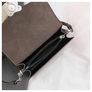 Detalle de bolso bandolera marrón mate con herrajes plateados y compartimento interior
