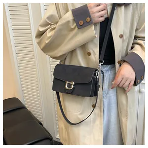 Bolso bandolera negro mate con hebilla plateada mostrado en modelo con gabardina