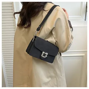 Detalle de bolso bandolera negro mate con hebilla en C plateada en modelo con gabardina clásica