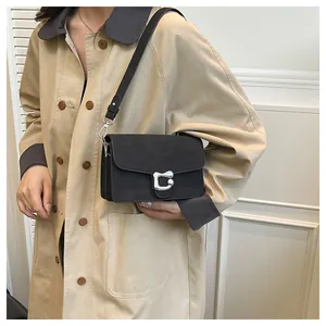 Detalle de bolso bandolera de ante negro con cierre en C plateado sobre gabardina beige