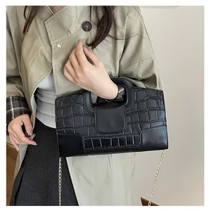 Detalle del bolso negro textura cocodrilo con asa troquelada y cadena dorada fina