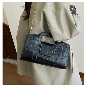 Detalle del bolso negro con relieve de cocodrilo y correa de cadena de metal dorado