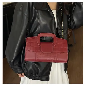 Detalle de bolso tote rojo oscuro con patrón de cocodrilo y cadena dorada en modelo