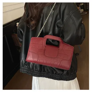 Detalle de bolso tote burdeos con grabado de cocodrilo y cadena dorada en modelo