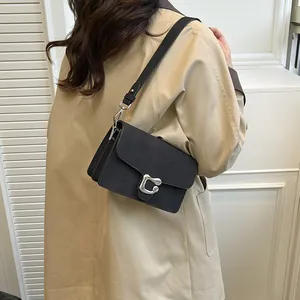 Bolso de hombro en cuero negro mate con hebilla plateada vintage sobre una gabardina beige