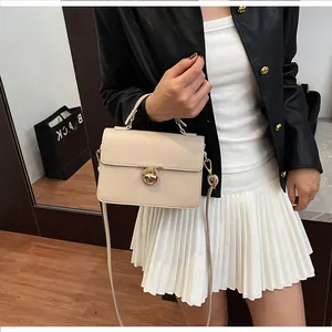 Détail du sac à main beige à motif litchi avec fermoir doré sur une tenue de mannequin