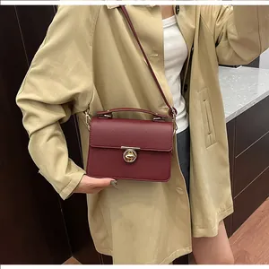 Détail du sac à main en cuir grainé bordeaux avec fermoir doré porté par le modèle