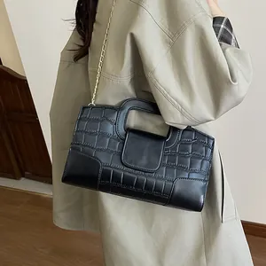 Bolso tote negro con relieve de cocodrillo y cadena dorada sobre una gabardina caqui