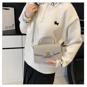 Détail d'un sac à main gris en cuir grainé avec nœud et fermoir doré sur l'épaule