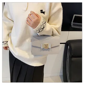 Gros plan du sac à main en cuir gris clair avec fermoir nœud doré et texture grainée