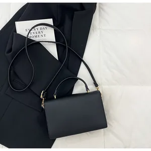 Détail d'un sac à main noir grainé avec ferrures dorées sur fond de costume élégant