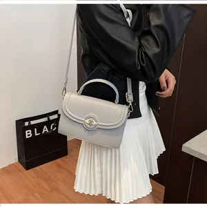 Détail d'un sac à main gris en cuir grainé avec fermoir doré sur une robe blanche