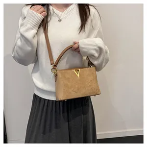 Bolso de ante marrón con logotipo V dorado, combinado con un suéter blanco elegante