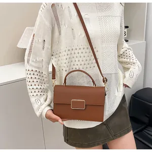 Détail du sac à main marron texture litchi avec boucle dorée porté par un mannequin
