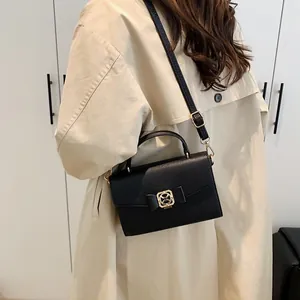 Sac à main noir grainé avec boucle nœud doré porté par un mannequin en trench beige