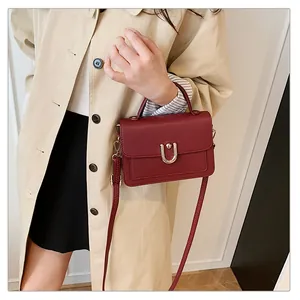 Détail du sac bandoulière bordeaux motif litchi avec fermoir doré et trench-coat beige