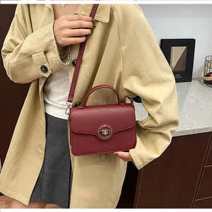 Détail du sac à main bordeaux en cuir avec fermoir doré sur un trench-coat beige