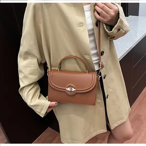Détail d'un sac à main en cuir grainé marron avec fermoir doré porté par un mannequin