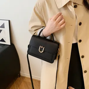Sac à main élégant en cuir noir grainé avec boucle en U dorée sur un manteau kaki