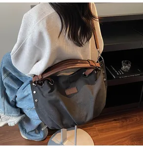 Vista detallada del bolso tote de lona oscura con correas de cuero marrón y remaches de metal