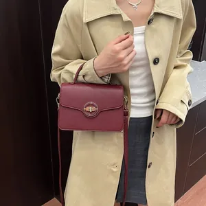 Sac à main bordeaux en cuir grainé avec fermoir doré porté sur un trench-coat élégant