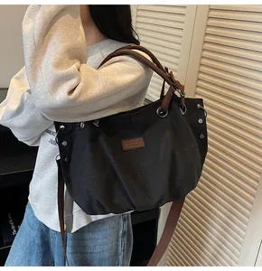 Modelo luciendo bolso tote grande de lona negra con correas marrones y detalles metálicos