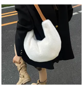 Détail d'un sac demi-lune en peluche blanche avec bandoulière en cuir sur blazer noir