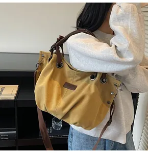 Detalle del bolso tote de lona amarilla con remache lateral y decoración de ojales metálicos