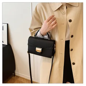 Détail d'un sac à main noir grainé avec boucle dorée porté sur un trench-coat beige