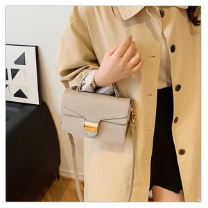Détail du sac à main gris clair motif litchi avec fermoir doré sur un trench-coat beige