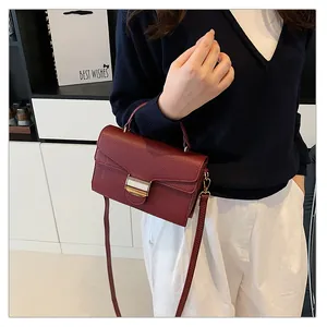 Détail du sac à main bordeaux en cuir grainé avec boucle dorée porté par un mannequin