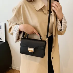 Sac bandoulière noir texture litchi avec fermoir doré porté par un mannequin en trench