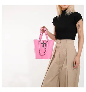 Detail of pink glossy bucket bag with metal cross and rivet decor on a model