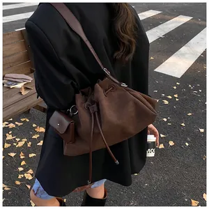 Dettaglio di una borsa a secchiello opaca marrone scuro con coulisse e pochette su una panchina