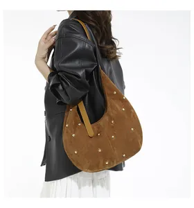 Sac demi-lune en daim marron avec clous dorés porté par un mannequin élégant