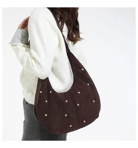 Sac hobo mat marron foncé avec clous dorés porté à l'épaule pour les détails de taille